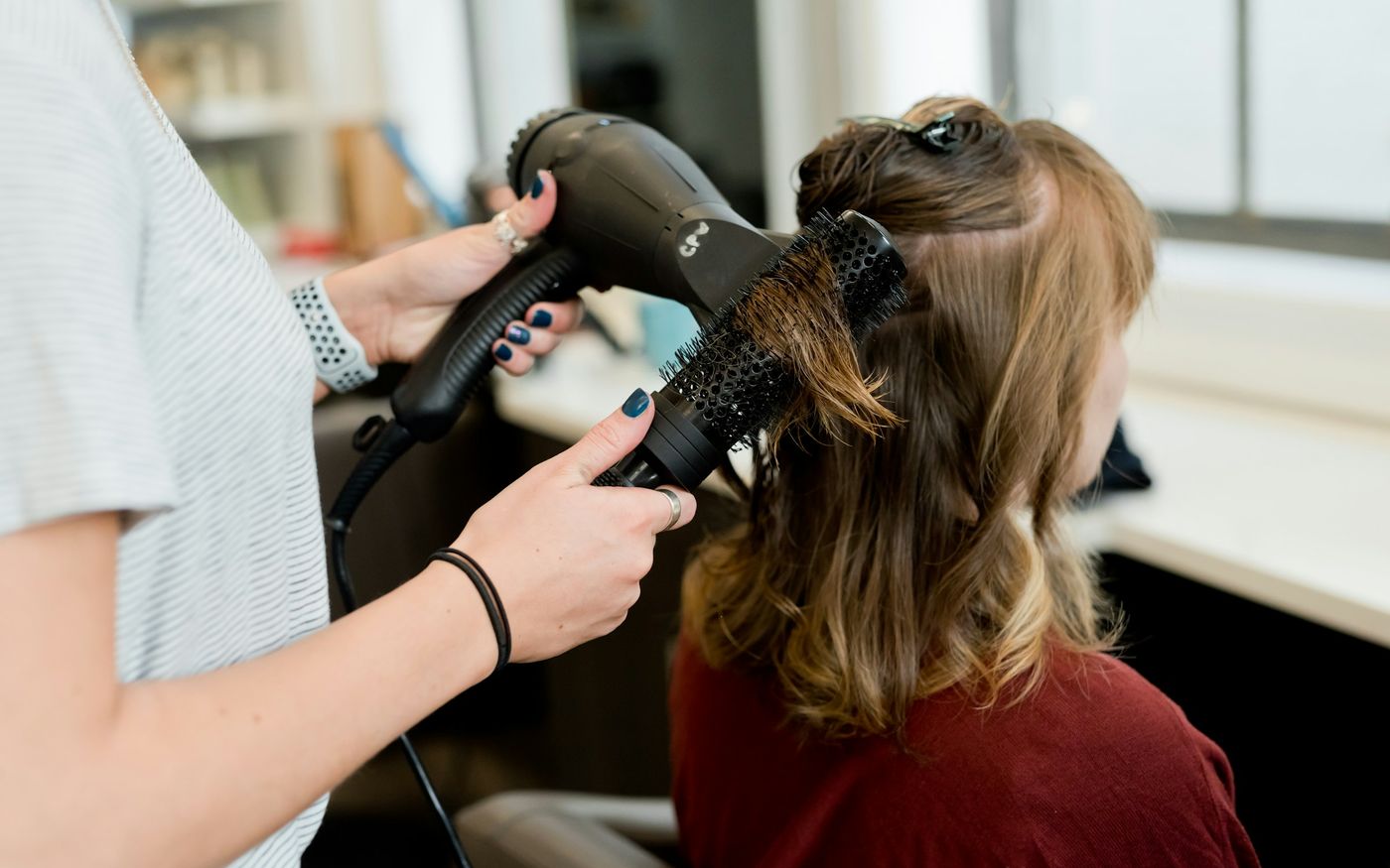 Une coiffeuse sèche les cheveux d'une cliente au sèche-cheveux et à la brosse ronde.
