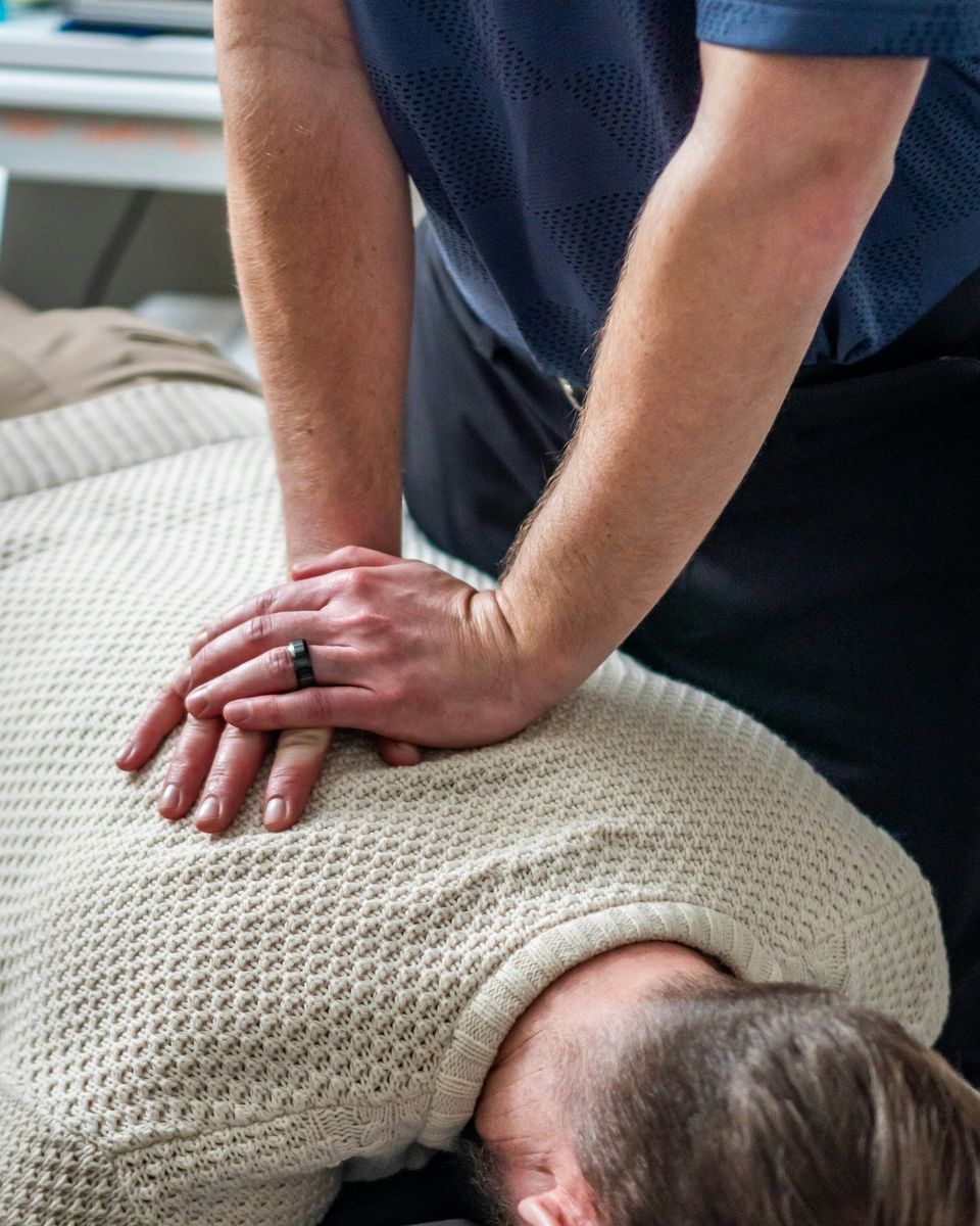 Un praticien pose les mains sur le haut du dos d'un patient allongé, en séance.