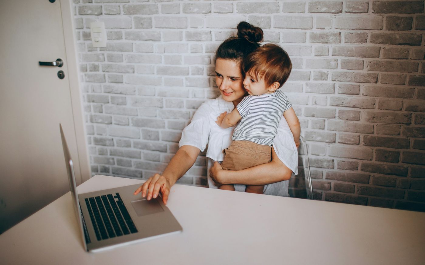 Une mère tient son enfant dans les bras et tape de l'autre main sur un ordinateur portable.