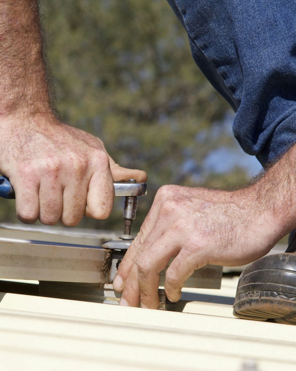 Les mains d'un couvreur fixent une tôle sur un toit, une clé à cliquet en main.